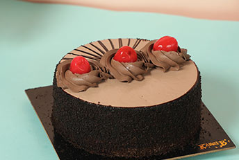 Kabhi B's rich chocolate cake, elegantly decorated with cherries and chocolate swirls.