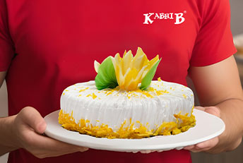 A beautifully crafted Kabhi B cake, adorned with fresh white frosting, vibrant yellow and green floral decorations, and golden crumbs for a delightful touch