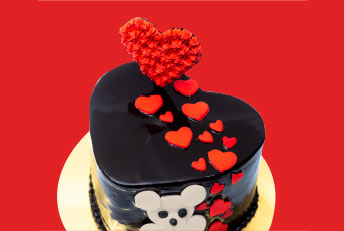 A beautifully designed heart-shaped Kabhi B cake, featuring a glossy chocolate glaze, red heart decorations, and a charming teddy bear motif